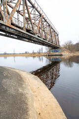 A metal truss bridge over the river in overcast spring day. Natural springtime scenery in Riga,...