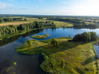 Fototapeta premium A beautiful summer landscape of a small lake, green trees and fields, taken from a drone. Natural rural landscape of Latvia, Northern Europe.
