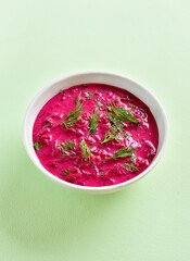 Cold summer beetroot soup in bowl over green background