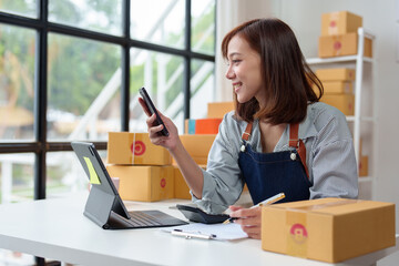 Small business startup, SME owner, female entrepreneur working on parcel boxes Receipt and check online orders via mobile phone in order to prepare boxes for sale to customers. Online SME concept.