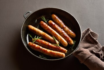 Delicious thin sausages in frying pan on dark background