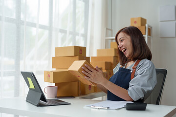 SME entrepreneurs, small businesses Online sales concept, happy Asian female business owner working on laptop computer and parcel boxes. Delivery of SME parcel boxes to customers Confirm order.