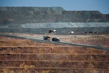 Yellow trucks drive out a dirt road in an open cast mine in New South Wales, Australia. Gold Mine.