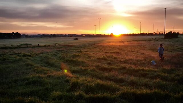 Sunrise behing woman walking dogs through farm grass