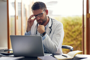Obraz premium Male person, physician and laptop with thinking, ideas and planning in office as medical doctor. Man, pediatrician and diagnosis, telehealth and technology for patient records, medicine or surgery