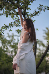 Naklejka premium A woman in a white outfit stretches her arms upwards, leaning against a tree. This image showcases the peaceful and harmonious interaction with the natural environment.
