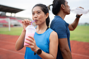 Portrait Mature runner Asia woman drinking pink milk and Asia man drinking pure water on racetrack	