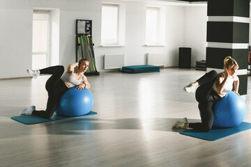 Two women perform exercise routines with fitballs in a gym setting.