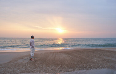 asian senior man tranquil standing alone at the beach,looking beautiful sunrise,concept of senior...