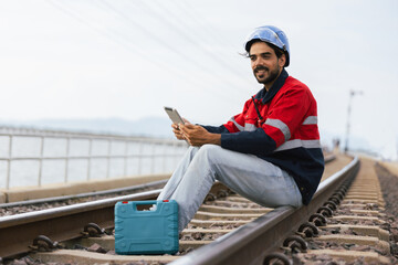 man in a red and blue jacket is sitting on a train track with a tablet in his hand