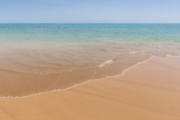 Front view of a small wave crashing on a sandy beach, sea and blue sky on a sunny day. Natural tropical travel and vacation background with copy space.