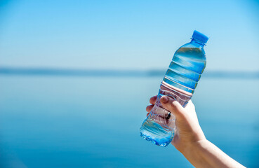A girl holds a bottle of drinking water in her hand against a blue sky background
