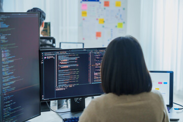 Asian software developers working on multiple screens displaying code and application diagrams in a...