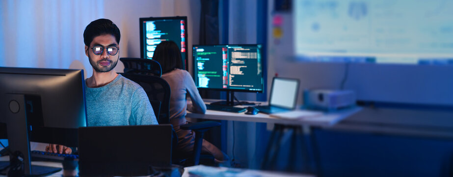 Asian software developers working on multiple screens displaying code and application diagrams at night in modern office