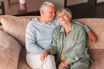 Portrait of a beautiful senior couple embracing each other, sitting on the couch at home