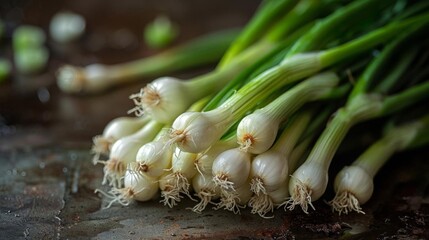 A close-up image of a bunch of fresh green onions. The onions are tied together with a rubber band. The background is a dark wood table.