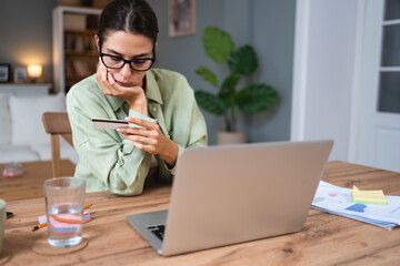 Simple living. Young woman sitting at home holding credit card having issue with online payment or...