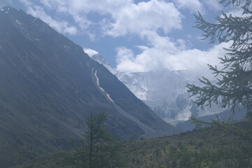 A captivating view of a green mountain slope with lush vegetation, distant peaks, blue sky, white clouds, and bright sunshine, creating an ideal setting for nature lovers and hikers.