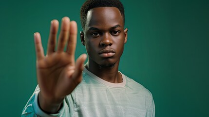 Obraz premium African american man holding hand forward giving signal to stop domestic violence, green isolated background with copy space. November 25 - International Day for the Elimination of Violence