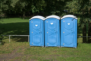Three blue mobile toilets in the park at an Open-Air festival event on the green meadow under trees...