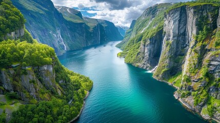 Obraz premium Dramatic panorama of a fjord with towering cliffs, lush green slopes cascading down to a crystal-clear turquoise sea.