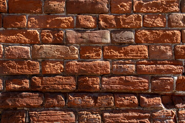 Obraz premium Fragment of a red brick wall, close-up. The texture of brick, battered by wind and rain. Old bricks in the wall of a building.