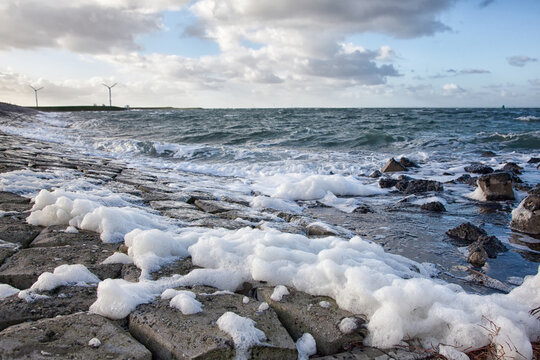 Schuimkoppen gevormd door de harde wind op zee slaan op de zeewering 