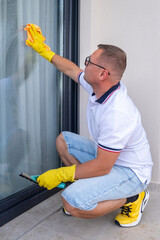 Man washing window on balcony, yellow gloves, rag and window scraper