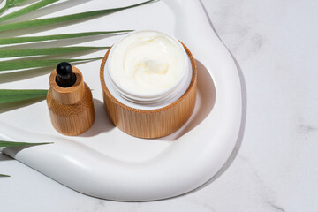 Cosmetics packaging. Set of different cosmetic jars and dropper bottle on white tray on marble background. Blank bamboo packaging. Natural beauty spa product concept. Beauty Mock-up