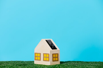 Miniature house with a solar panel on a grass patch against a blue sky