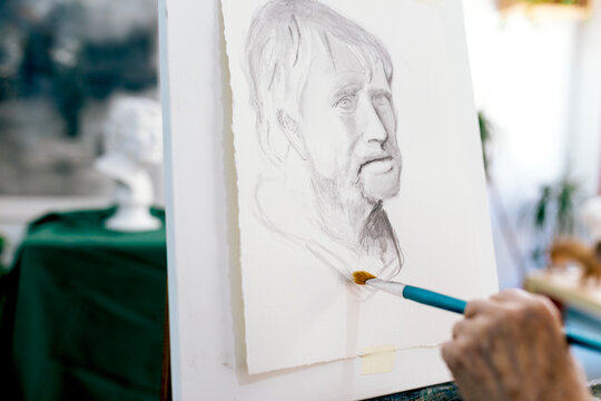 Unrecognizable elderly woman artist painting a portrait on canvas