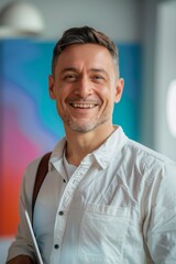 Obraz premium Portrait of a smiling man in a white shirt, holding a laptop, in a modern office setting