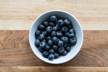 Top-down shot of fresh blueberries in a white bowl, set against a rustic wooden background. This image highlights the natural beauty and vibrant color of the blueberries. Healthy food
