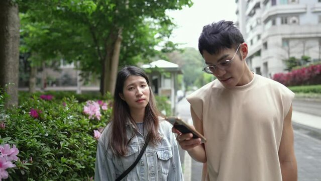 A young Taiwanese couple in their twenties walking through the streets of Xinyi District, Taipei City at noon in spring. The man is wearing a sleeveless top, and the woman is wearing a denim jacket.