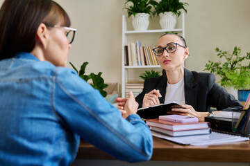 Confident female psychologist working with adult woman, sitting in office