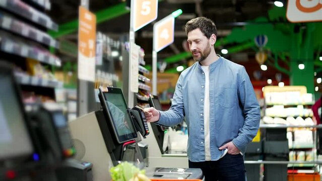 Male customer using a self-service cashier checkout in a supermarket. Shopper scanning produce items using at grocery store self serve cash register. cashier terminal man pay for products online
