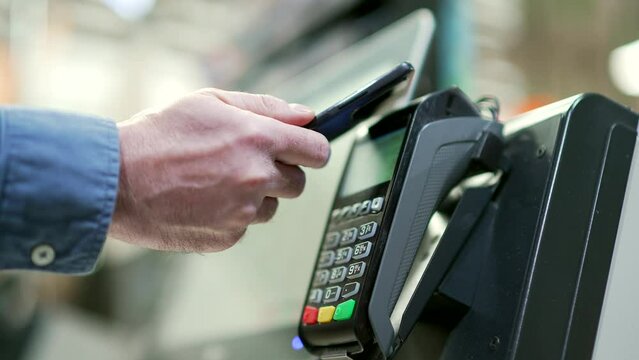 Close up man At Counter Buy electronic payment supermarket mall smartphone close-up male hand with mobile phone in hands pay paid for purchases in stores Contactless NFC Terminal Closeup card reader