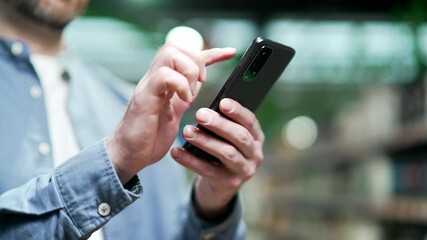 Сlose up male hand using smartphone communication with light bokeh standing indoor shopping center mall. Man in blue shirt use online store for discount, sale promotions using a mobile phone Closeup