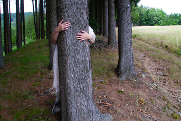 Spiritual woman with a scarf behind the tree hugging a tree in a forest, deep natural connection