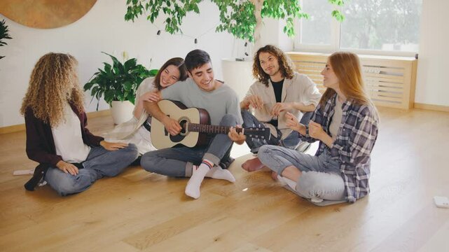 A group of young friends is having a wonderful time listening to acoustic music, singing, and bonding in a warm living room, creating a carefree and joyful atmosphere of togetherness and happiness