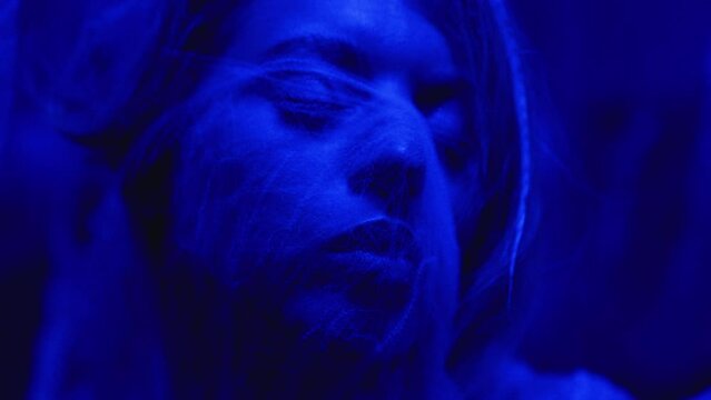 close up portrait of woman covered in cobweb standing in dark corridor illuminated by creepy blue light. scary and mysterious atmosphere suitable for halloween concept