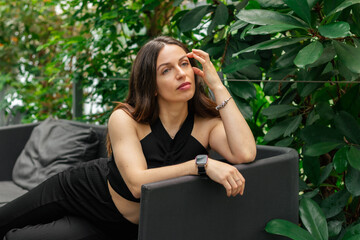 Beautiful woman in a greenhouse sitting on a sofa among green plants