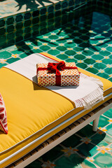 Christmas summer concept with xmas gift on sunbed deckchair. Vivid colors.