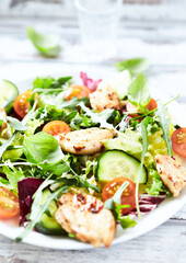 Salad with Chicken Breast, Cherry Tomatoes, Cucumber, Rocket and fresh Basil. Bright wooden background. Close up.