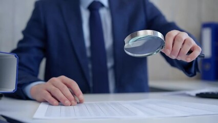 Businessman is carefully examining financial documents with a magnifying glass, highlighting the importance of thorough analysis in business. Audit and taxes