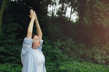 Korean girl stretches her hands to the sky for yoga meditates in the park. Unity with nature and...