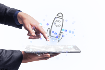 A person interacting with a digital tablet that projects a holographic rocket, symbolizing innovation or startup concepts, on a white background