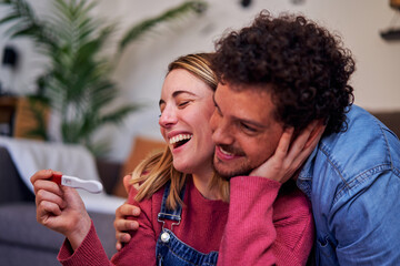 Caucasian couple finding out they are pregnant at home, looking at positive pregnancy test together...
