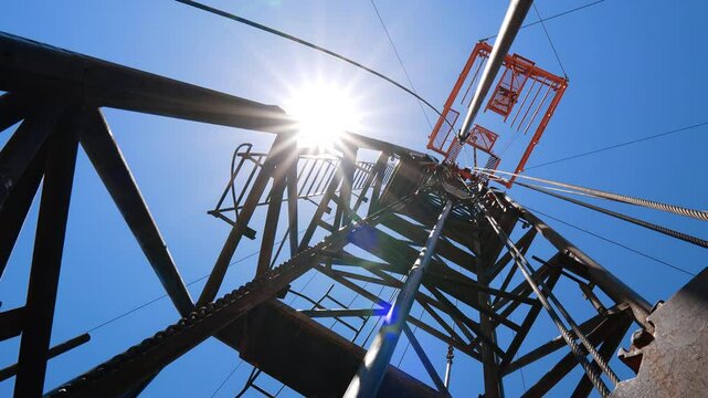 Standing at the foot of the metal tower used for drilling oil or gas. Low angle view on the derrick at resource producing site.