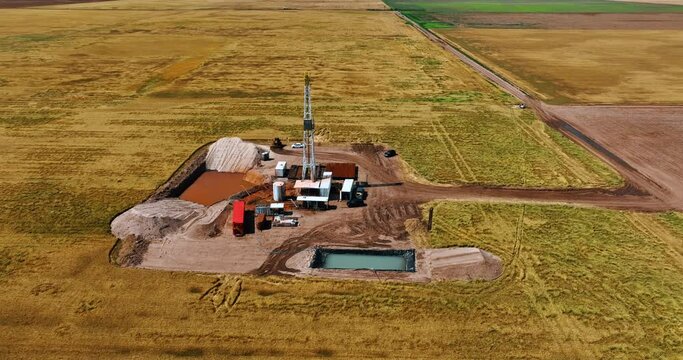 Flight around the small site for natural resources drilling in the vast field. Equipment and cars, two pools are at the location.